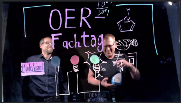 Zwei Personen hinter einer Glasscheibe, auf der in bunten Farben "OER Fachtag" geschrieben steht. Außerdem ist ein japanisches Schriftzeichen und ein chemisches Molekül erkennbar. 