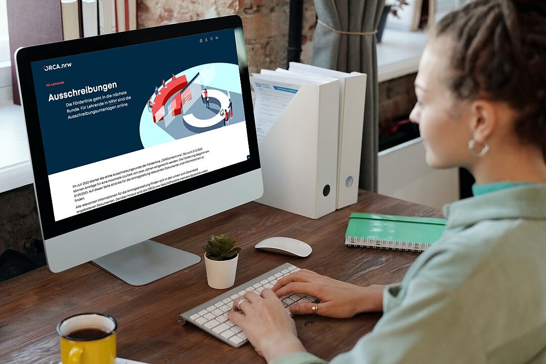 Eine Frau sitzt vor einem Computerbildschirm, darauf ist die Seite mit der Ausschreibung von OER Content auf der Webseite von ORCA.nrw zu sehen. 
